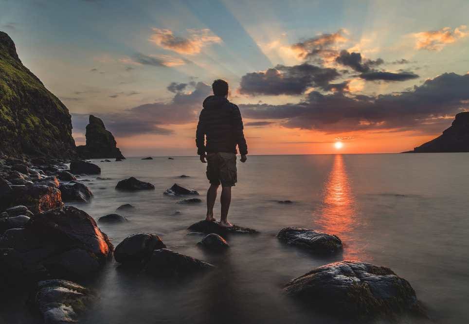 detall s'un viatger gaudint d'un capvespre des de la vora del mar