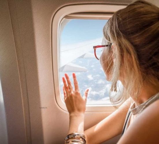 noia a l'interior d'un avió asseguda i mirant per la finestra