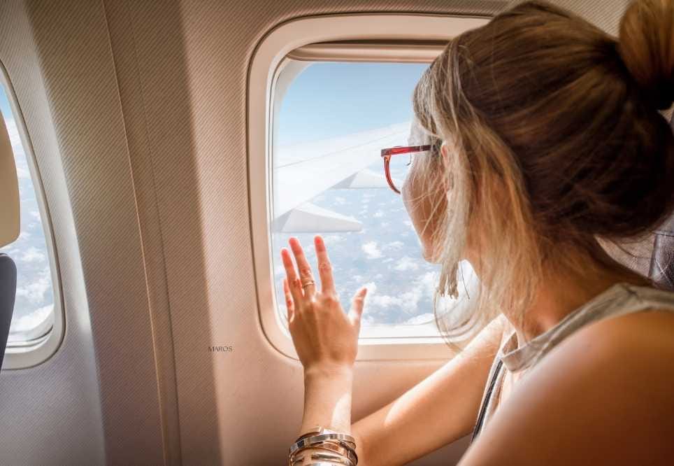 noia a l'interior d'un avió asseguda i mirant per la finestra